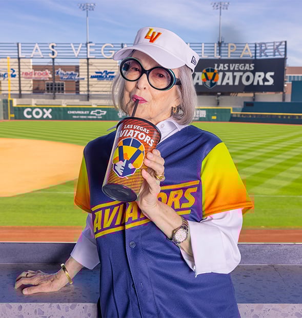 senior woman sipping a soda at a baseball park