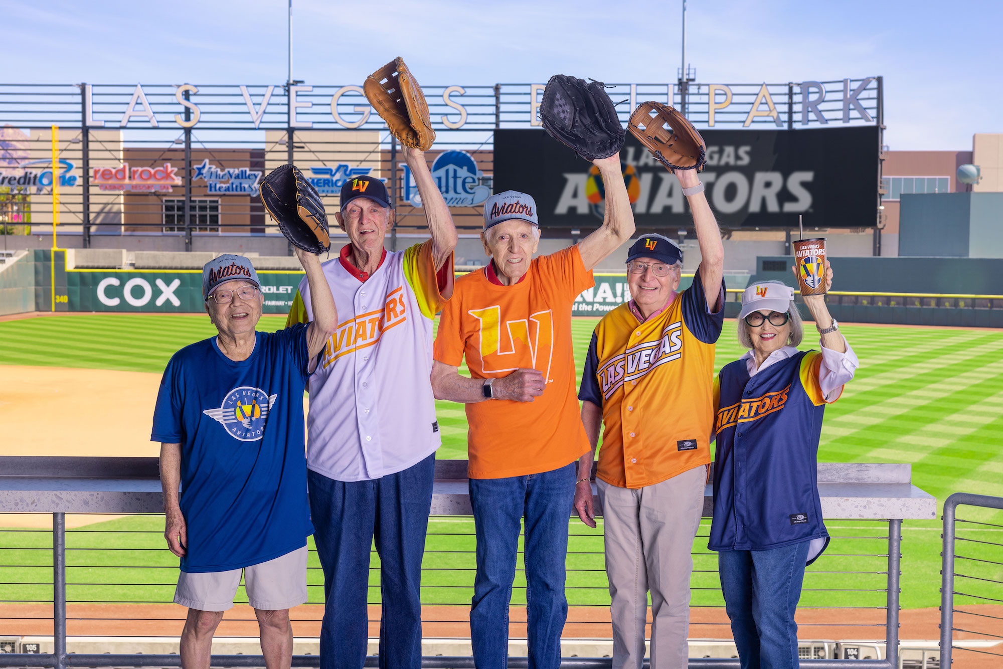 senior friends posing with baseball mitts at baseball field